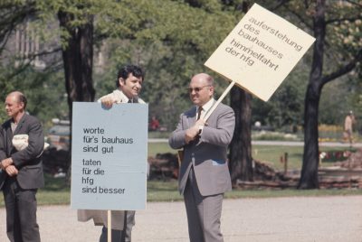 Zwei Männer, der eine mit großem Demonstrationsschild nach unten haltend und der andere das Demonstrationsschild nach oben haltend.